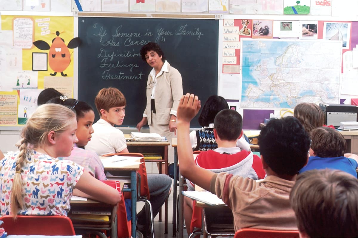 Pupils in a classroom, one raising a hand to answer a question