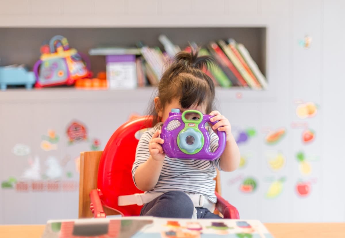 A young child playing happily with a toy camera in a bright playroom