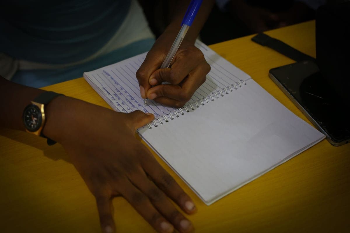 A young person writing notes in a ruled notebook during a Sunflower Foundation session